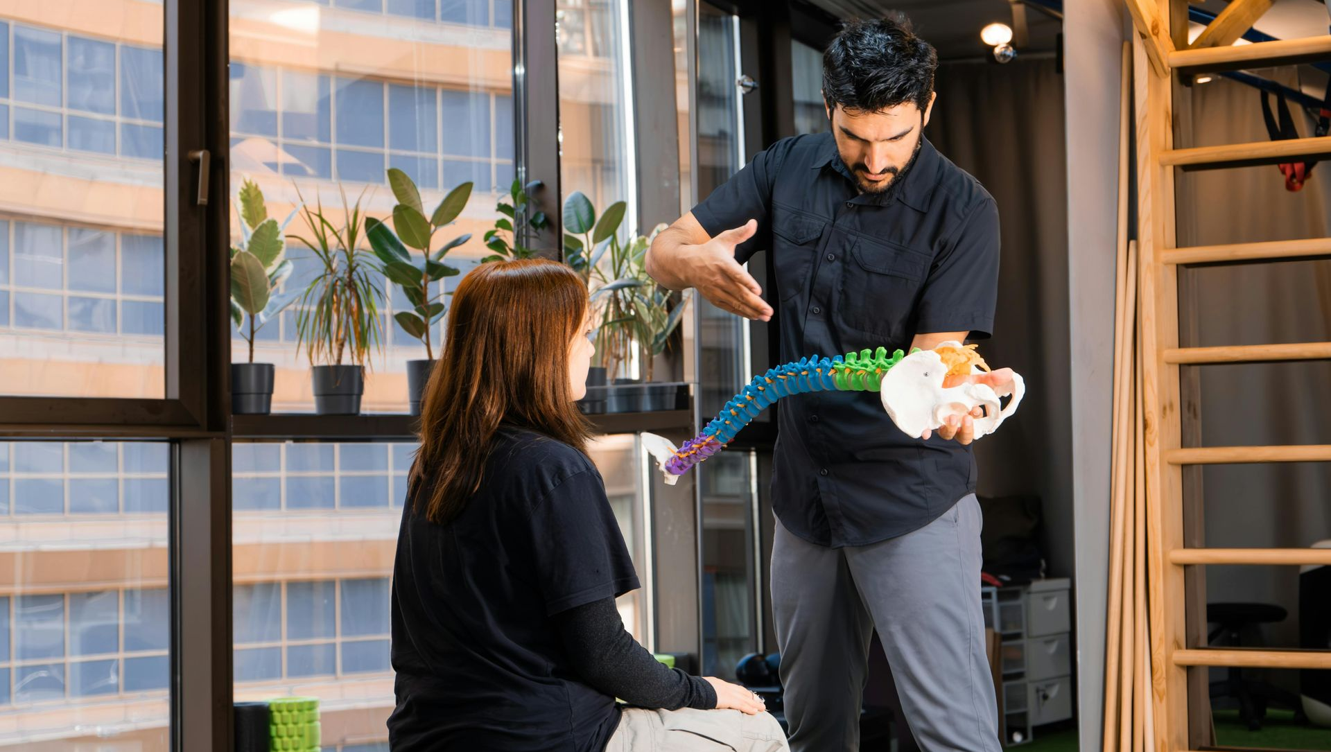A healthcare professional explains spinal structure to a patient, using a model in an office.