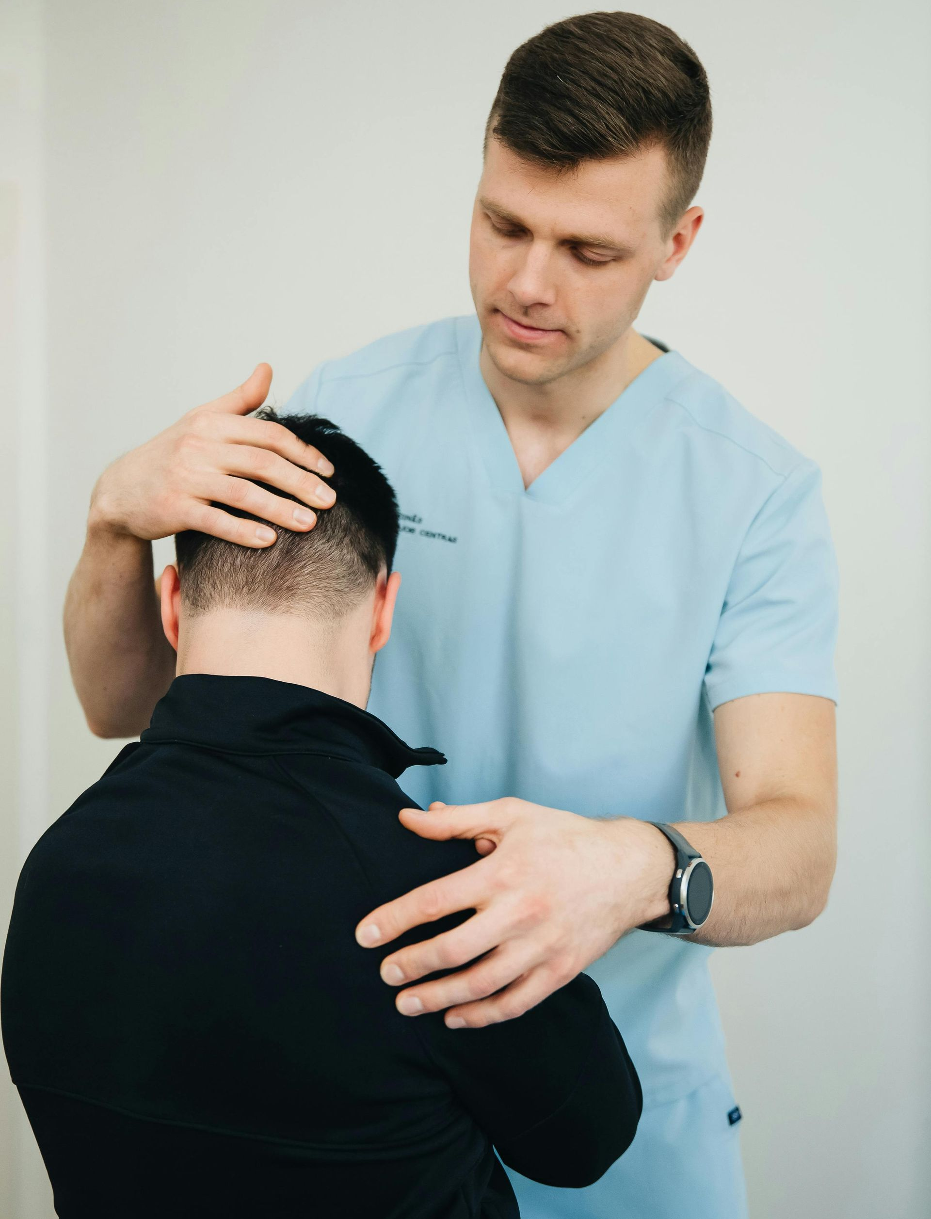 A medical professional examining a patient's head and shoulder; indoors.