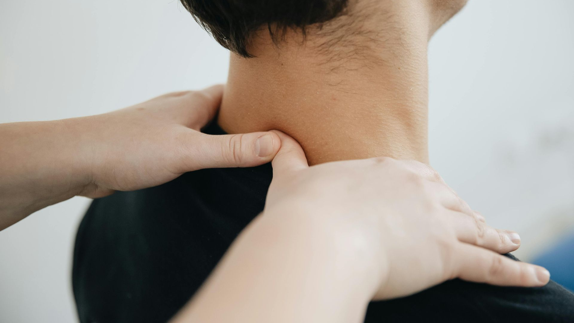 Hands massaging a person's neck and shoulders in a medical setting.