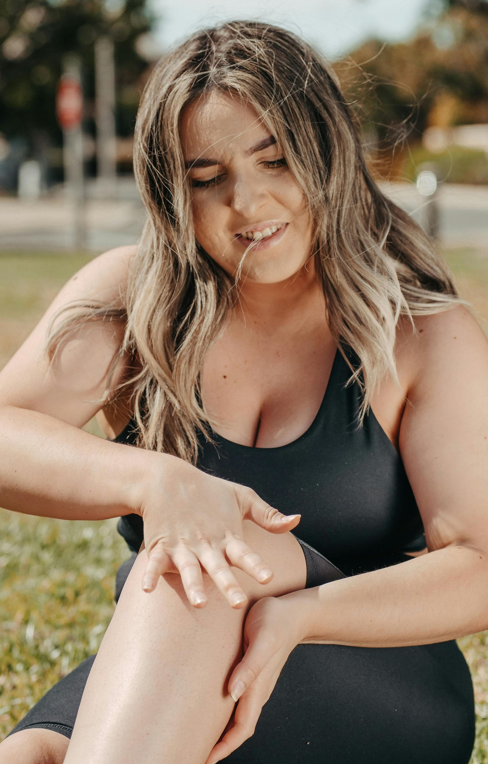 Woman in black athletic wear touches knee, sitting on grass outdoors.