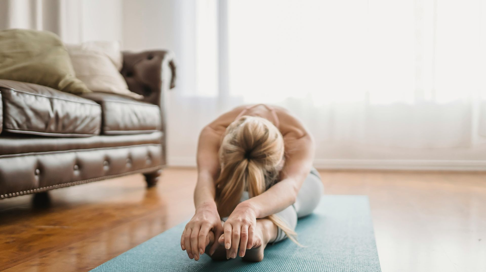 Woman stretching on a yoga mat; reaching towards toes; indoor setting.