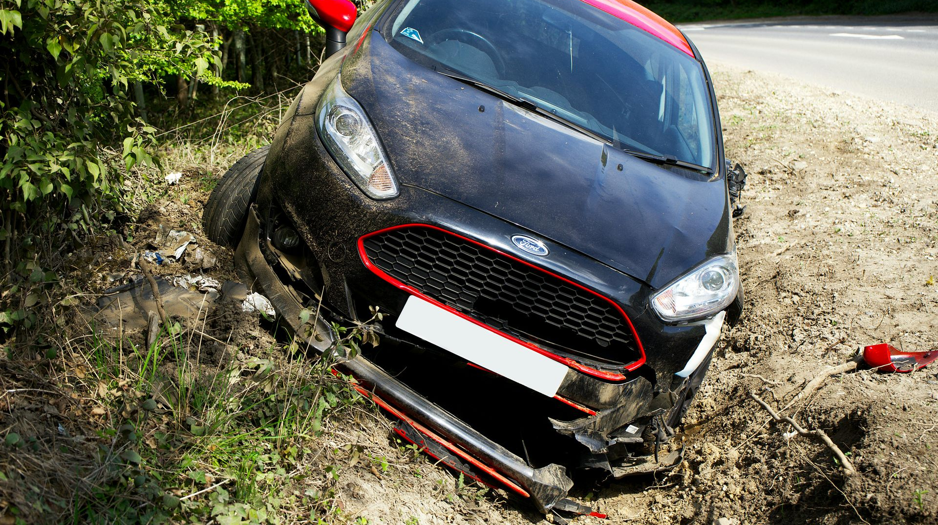 Black Ford car crashed off road into ditch, red accents visible.