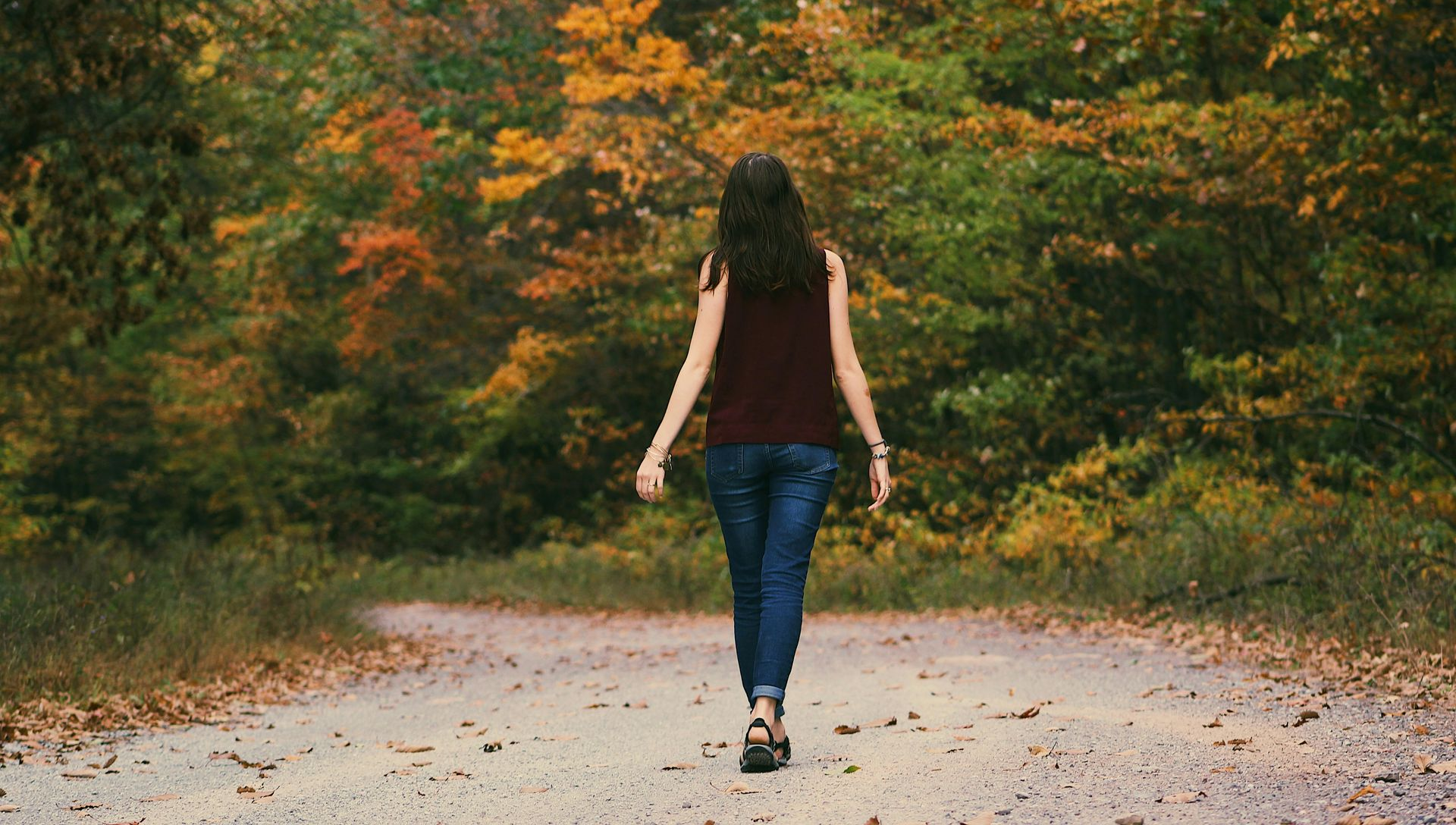 Woman walking away on a gravel path, surrounded by fall foliage.