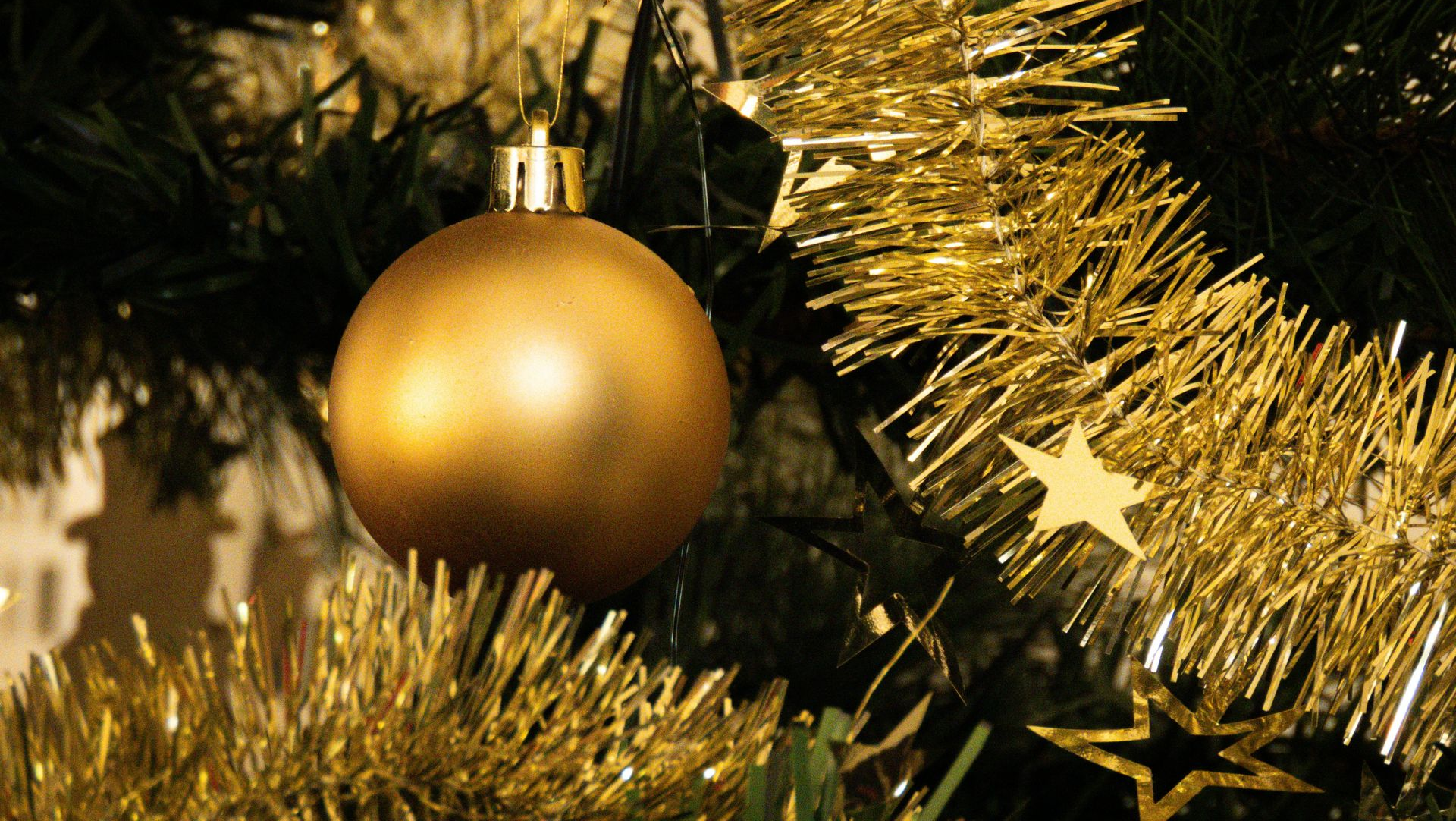 Gold Christmas ornament hanging on a decorated tree with gold tinsel and star decorations.