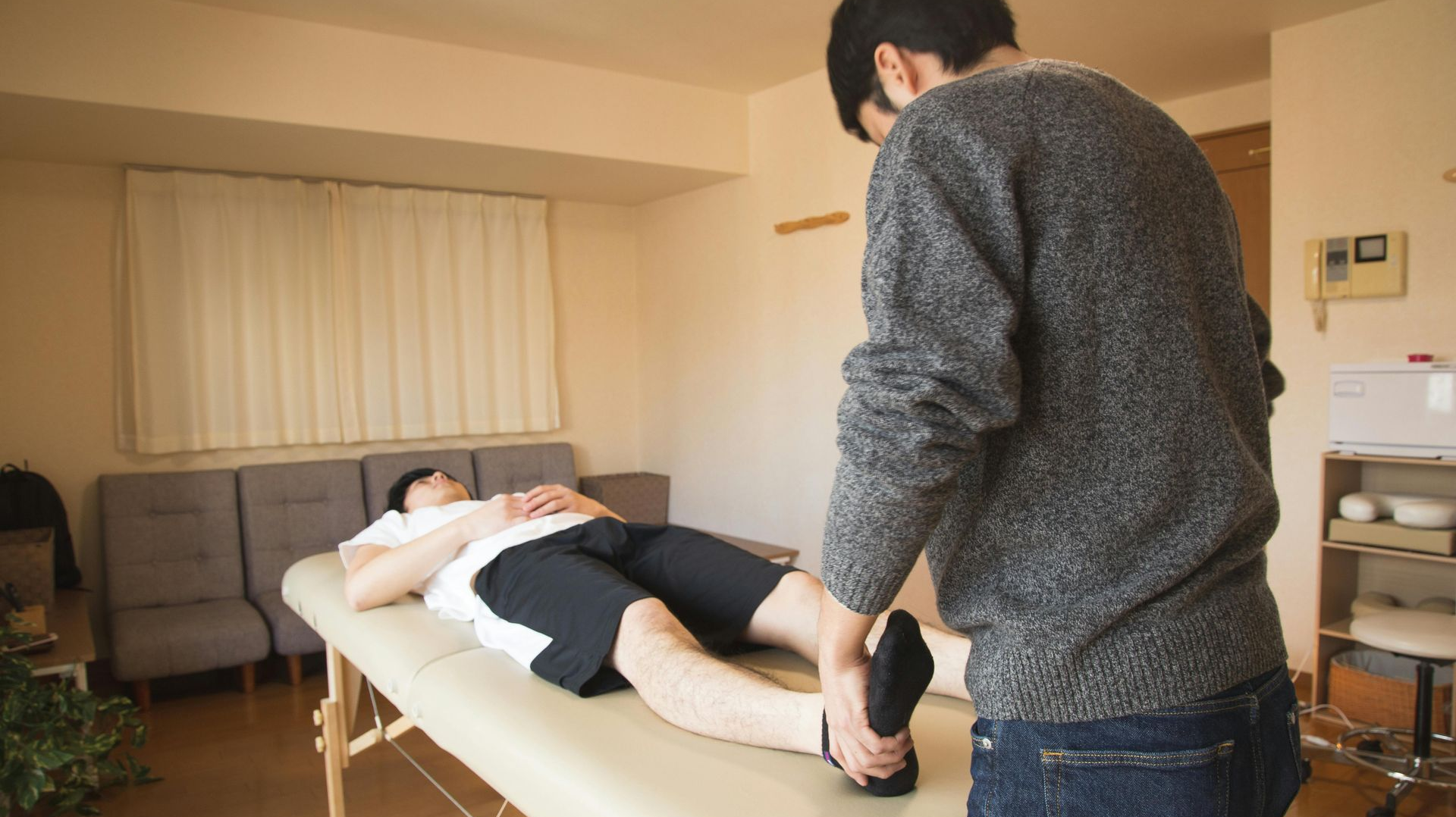 A person receives a foot massage while lying on a massage table indoors. Another person massages their foot.