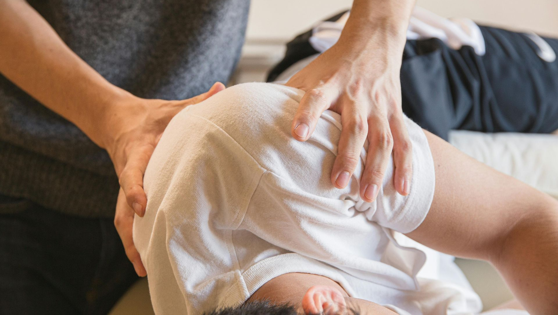 Hands massaging the shoulder of a person lying down, indoor setting.