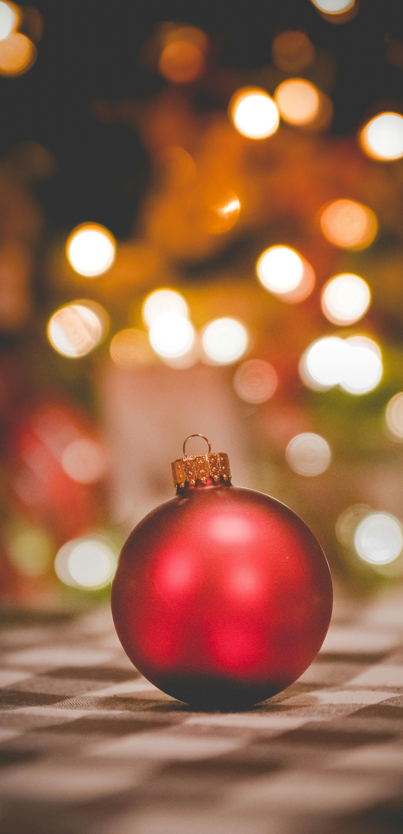 Red Christmas ornament on a checkered surface, with blurred lights in the background.