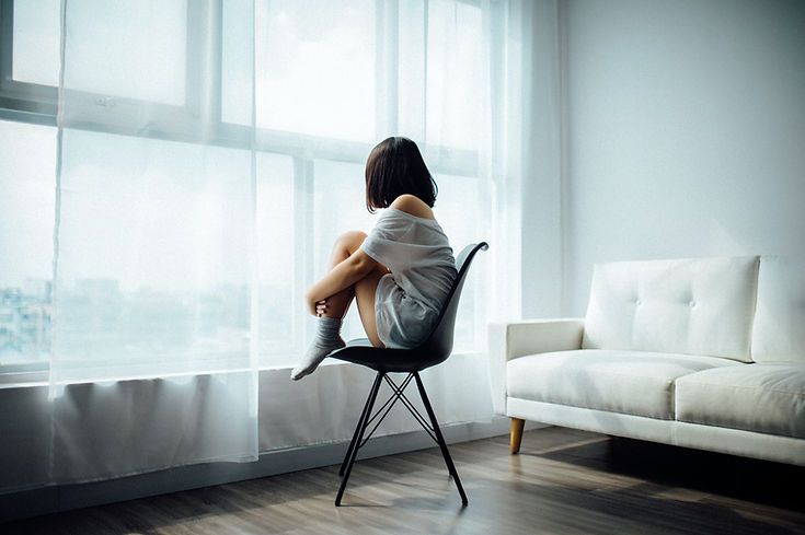 A woman is sitting in a chair looking out of a window.