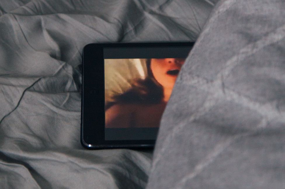 A cell phone is laying on a bed with a picture of a woman on the screen.