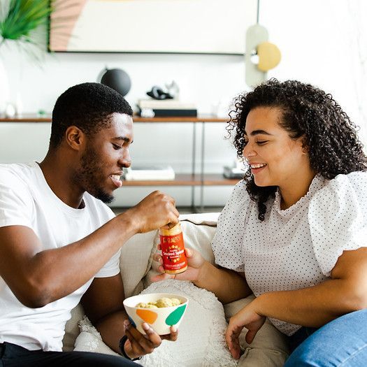 A man and a woman are sitting on a couch eating food.