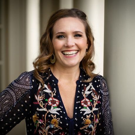 A woman in a floral embroidered shirt is smiling for the camera.