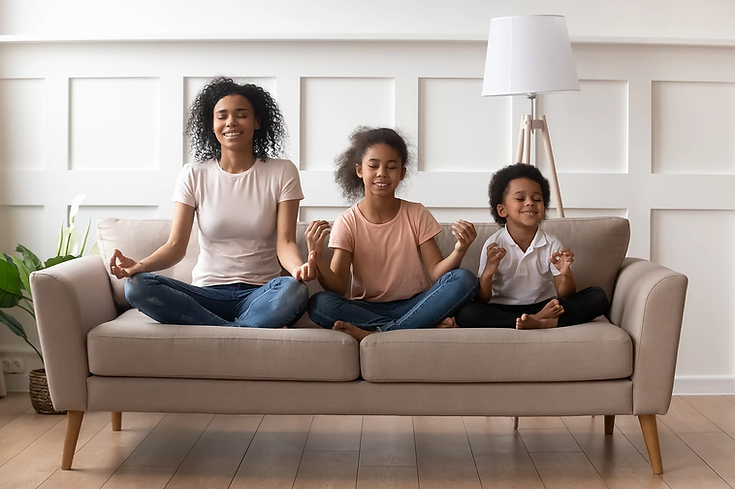 A woman and two children are sitting on a couch meditating.