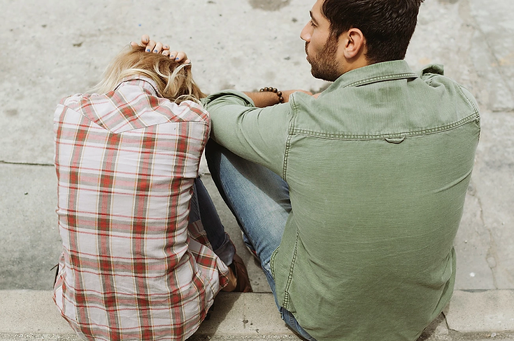 A man and a woman are sitting on the sidewalk.