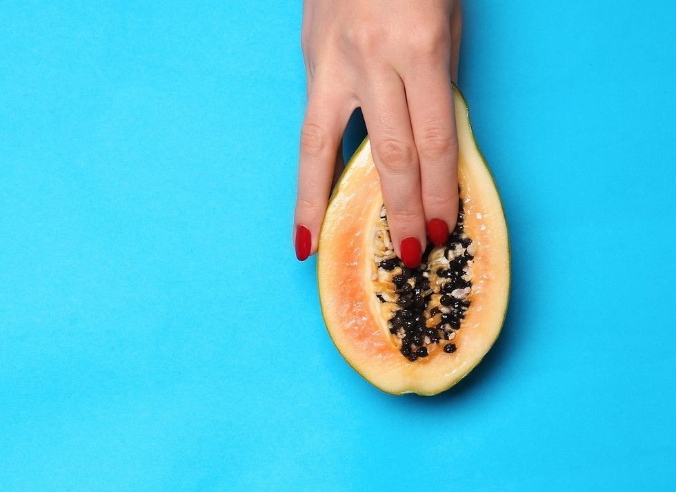 A woman 's hand is holding a half of a papaya on a blue background.