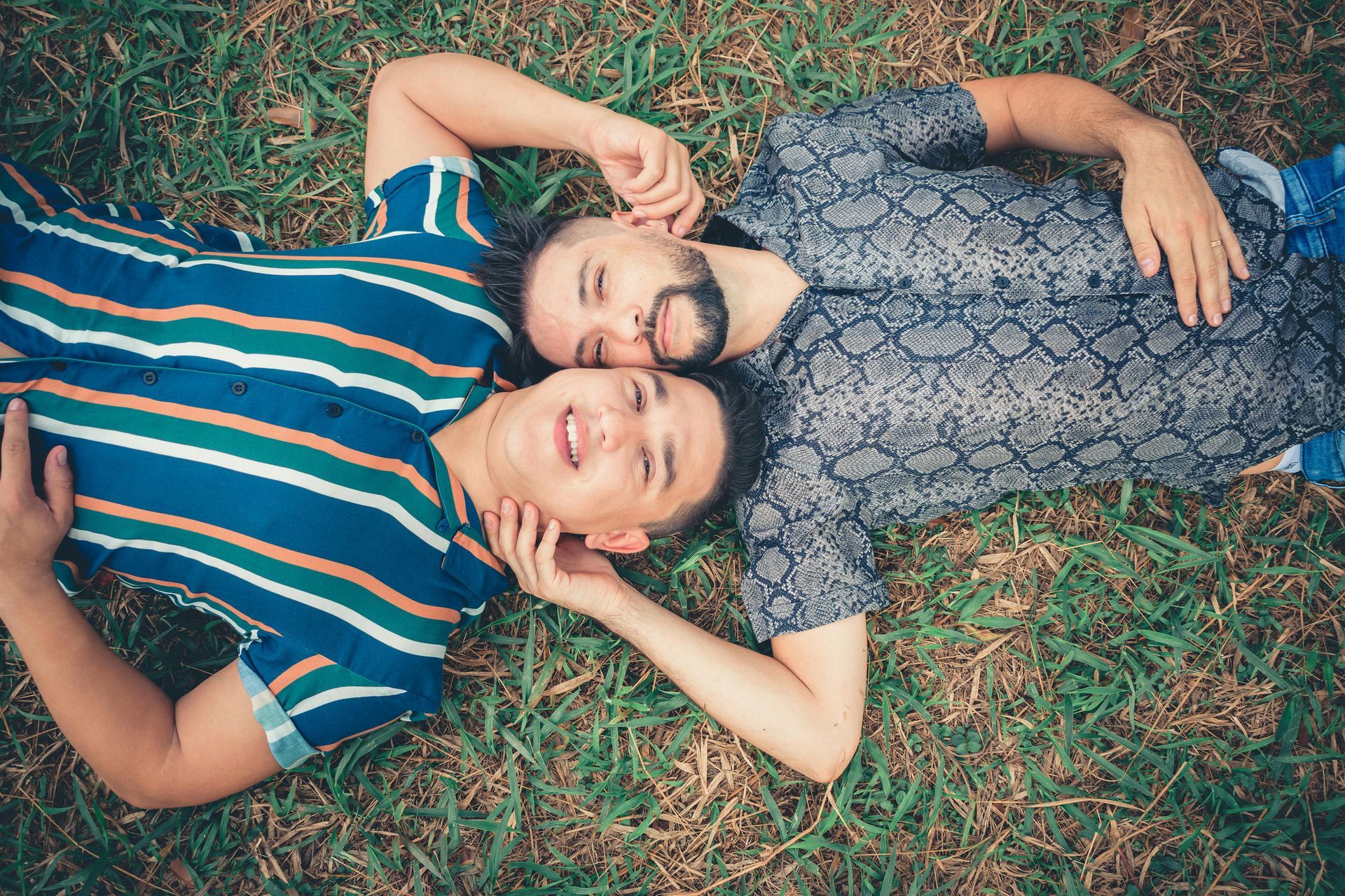 Two men are laying on top of each other in the grass.