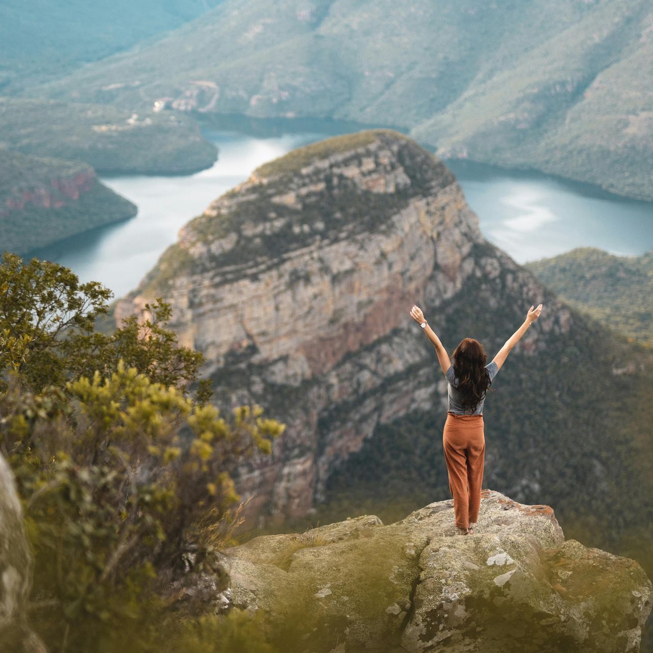 A woman is standing on top of a mountain with her arms outstretched.