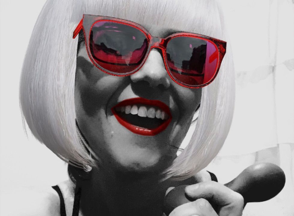 A woman wearing red sunglasses and red lipstick is smiling