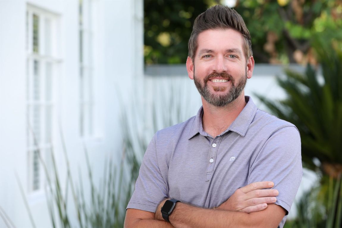 a man with a beard is standing with his arms crossed in front of a white building .