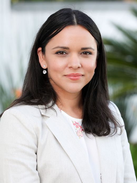 a woman with long dark hair is wearing a white jacket and earrings .