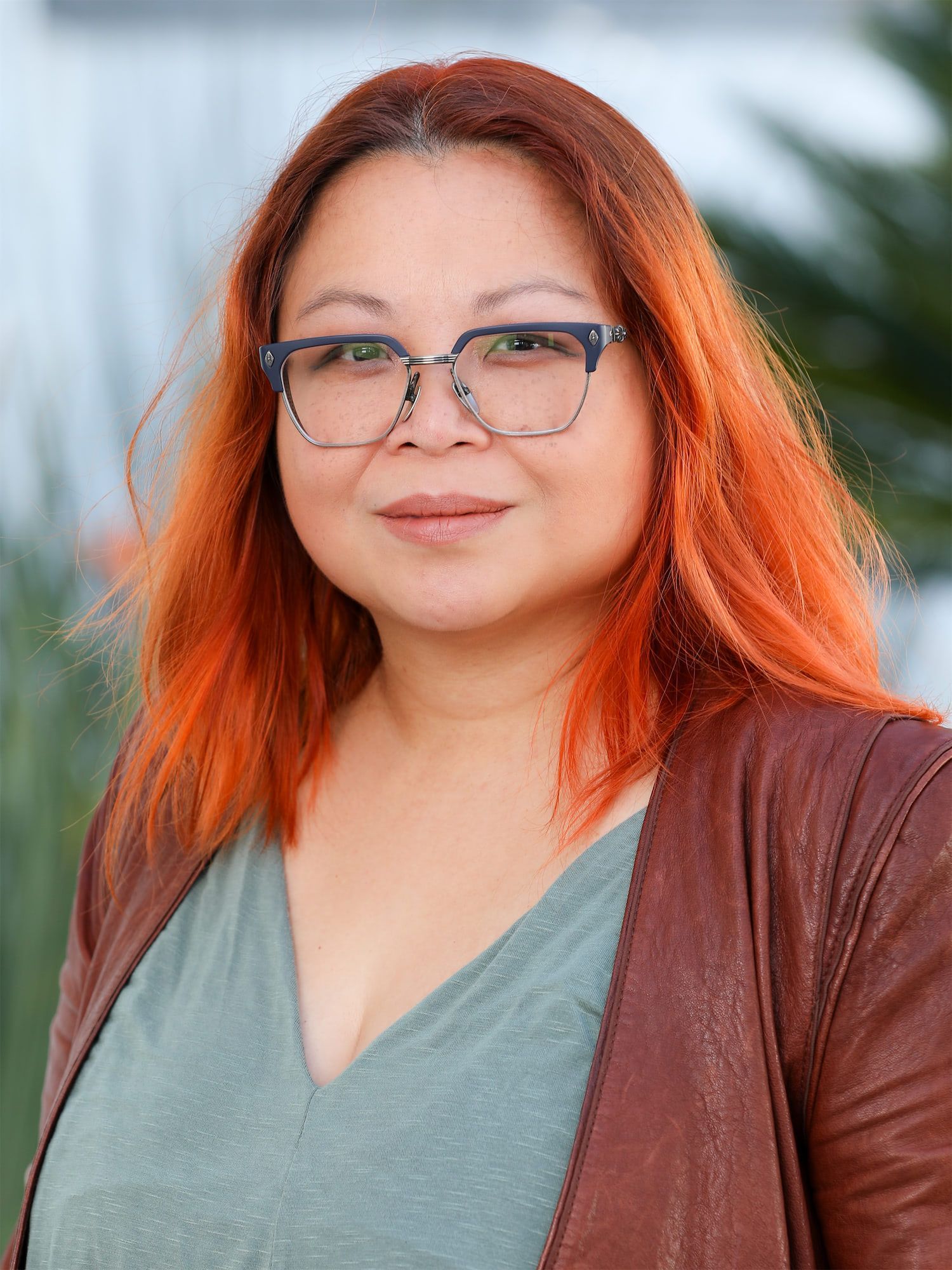 a woman with red hair and glasses is wearing a brown jacket and a green shirt .