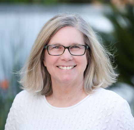 a woman wearing glasses and a white sweater is smiling for the camera .