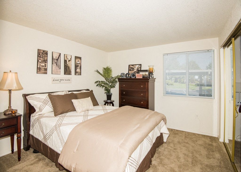 Bedroom in an apartment with a queen bed, nightstands, dresser, and a window.