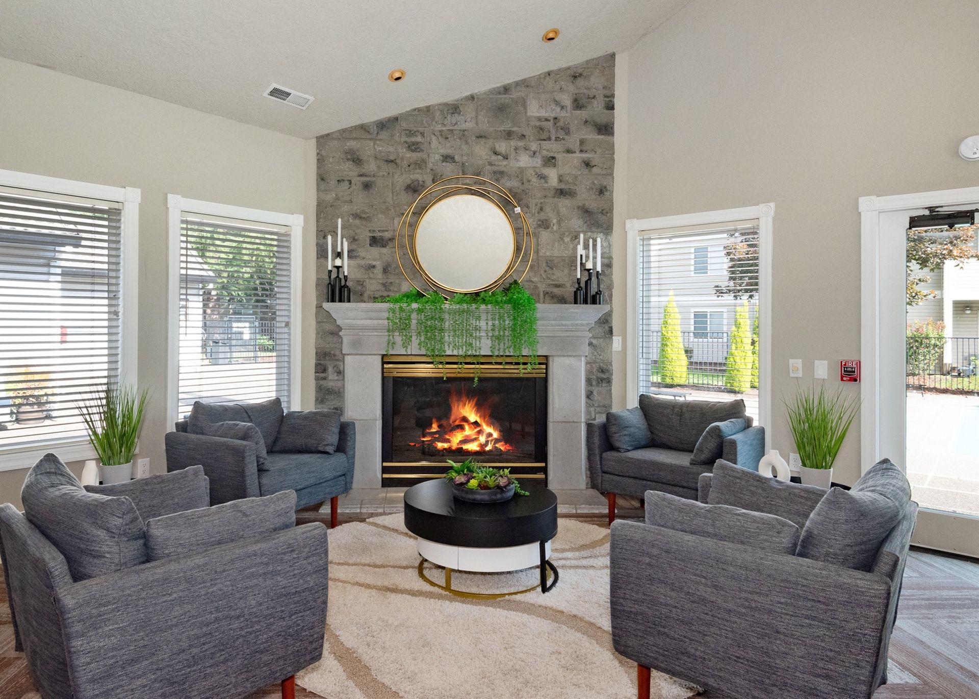 Living room with a stone fireplace, gray seating, and large front windows.