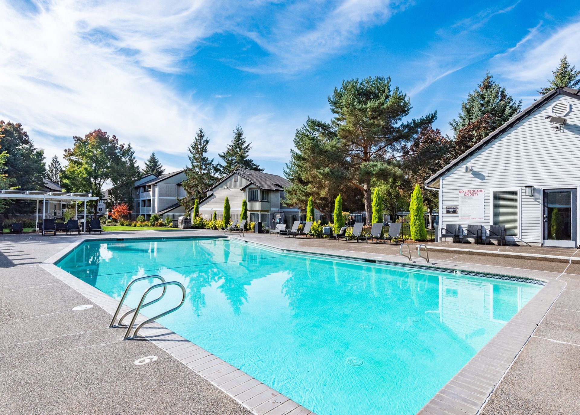 Outdoor apartment community pool with lounge chairs and surrounding trees.