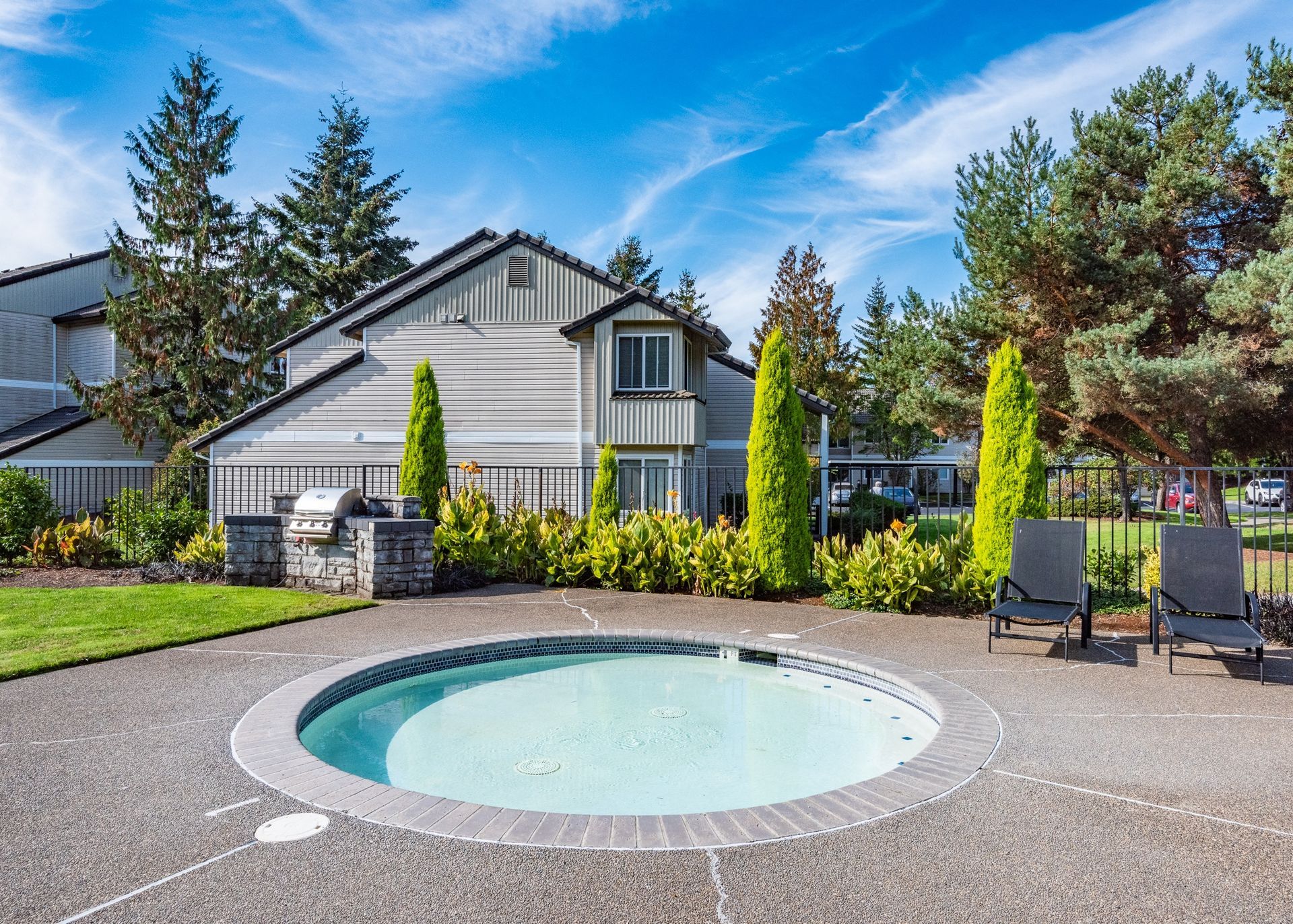 Circular outdoor pool with two lounge chairs, surrounded by plants and a fence.
