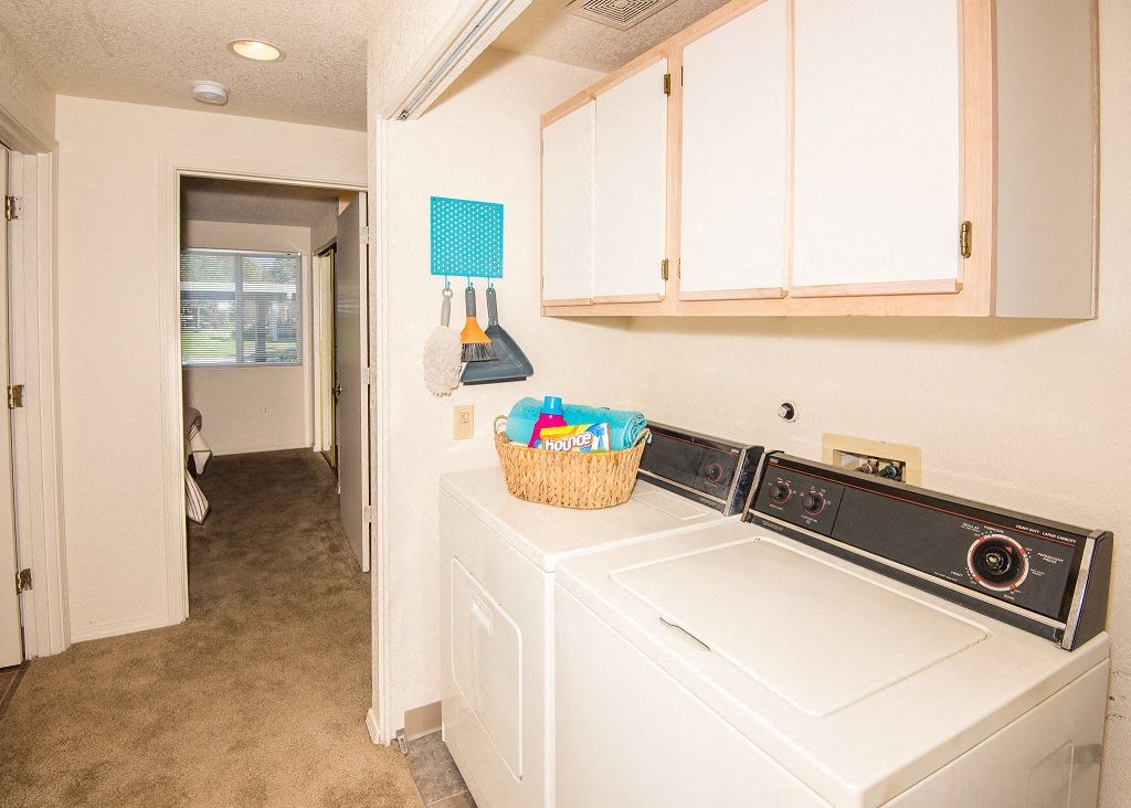 Laundry room with a washer and dryer, white cabinets above, and a hallway to a bedroom.