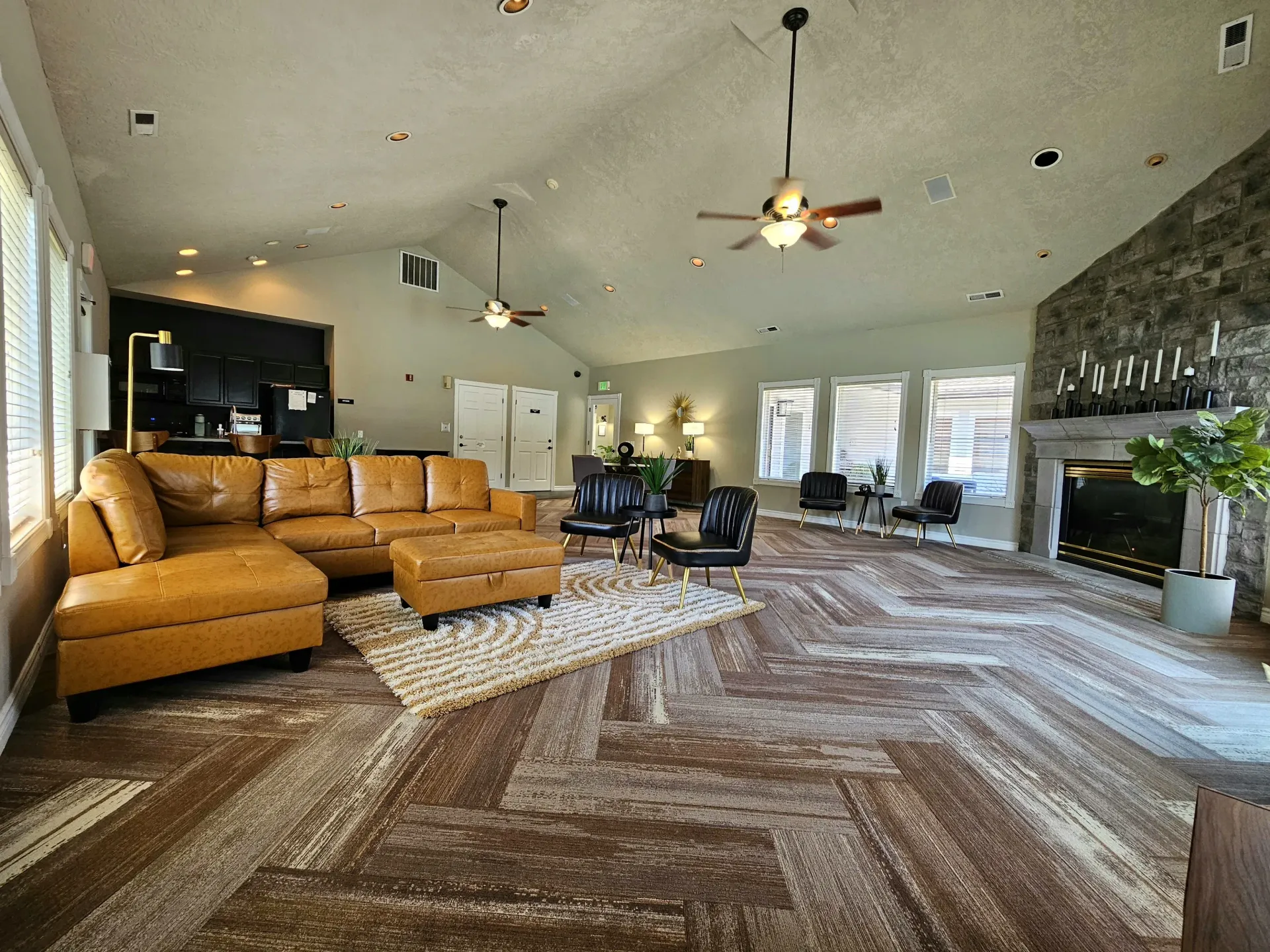 Spacious community living room with tan sectional, black chairs, and a stone fireplace.