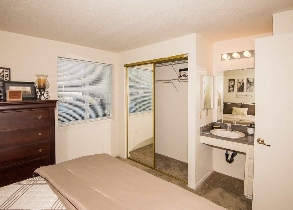 Bedroom in an apartment with a mirrored closet, dresser, window blinds, and a sink vanity.