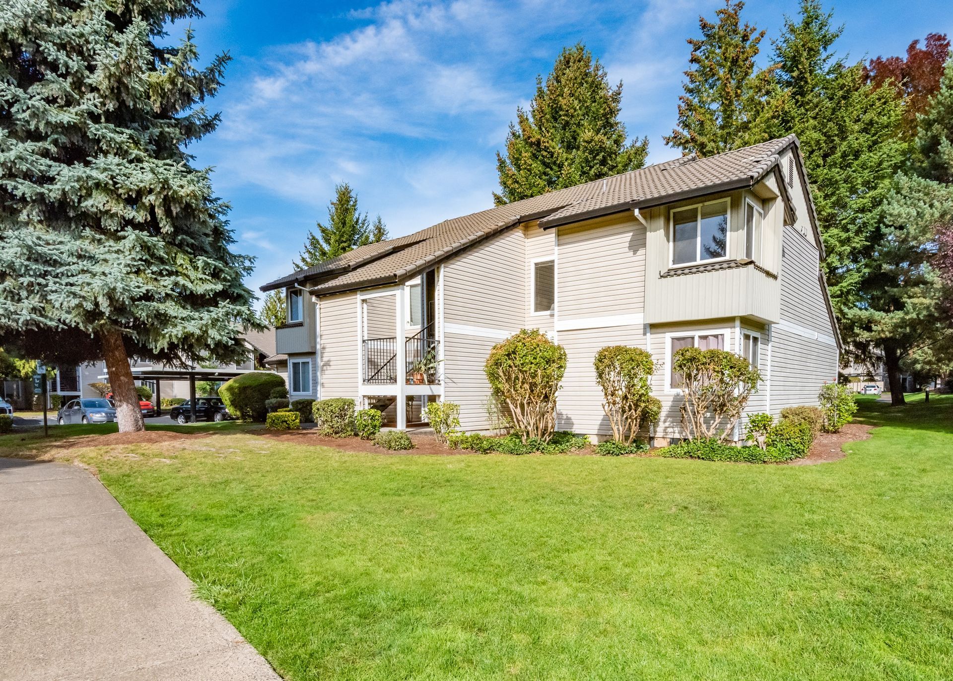 Exterior view of a beige, multi-family building with green lawn and trees.
