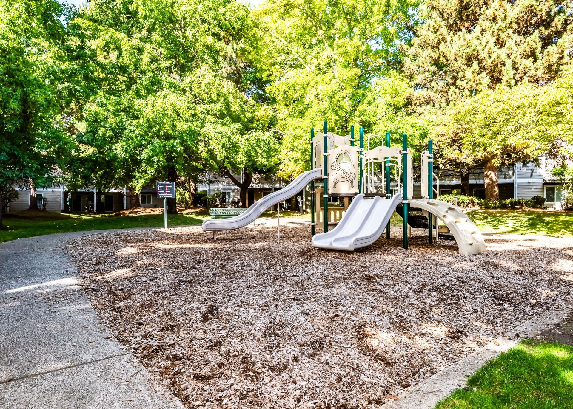 Playground with slides and climbing structure surrounded by green trees at an apartment community.