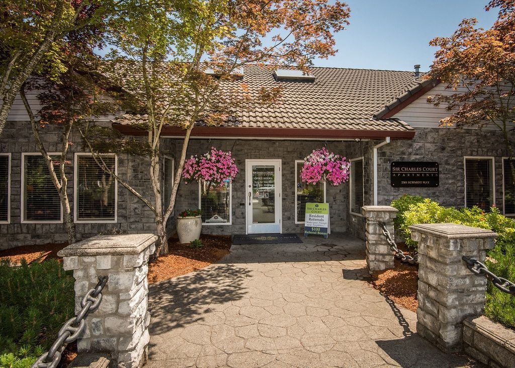 Exterior entrance to a stone-clad apartment community with hanging flower baskets.