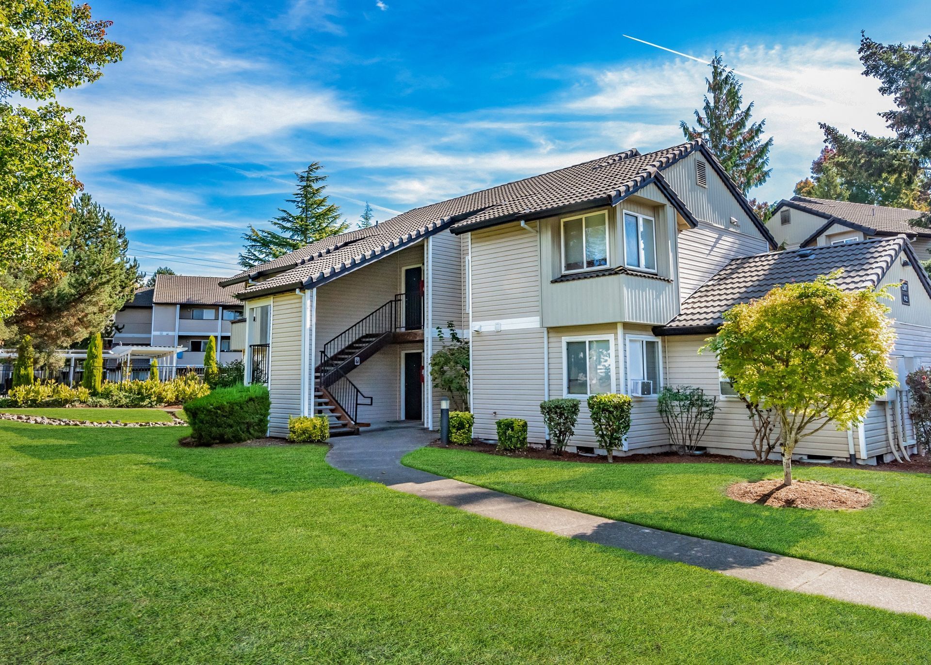 Exterior view of a multi-family apartment building with green lawn and a sidewalk.