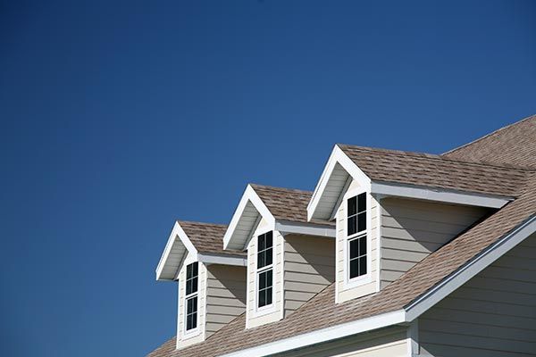 The roof of a house with three windows and a blue sky in the background.