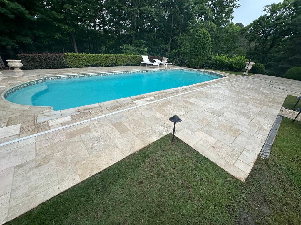 There is a large swimming pool in the backyard surrounded by trees.