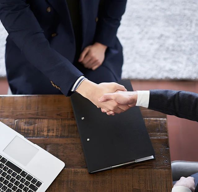 A man in a suit shakes hands with another man in front of a laptop