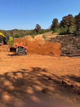 A bulldozer is moving dirt in a field with trees in the background.