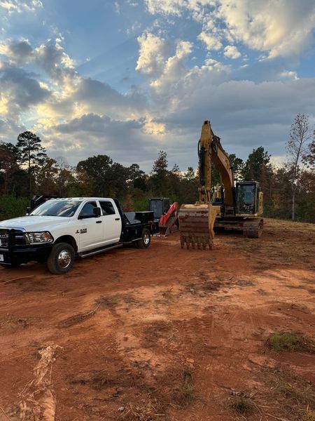A white truck is parked next to an excavator in a dirt field.