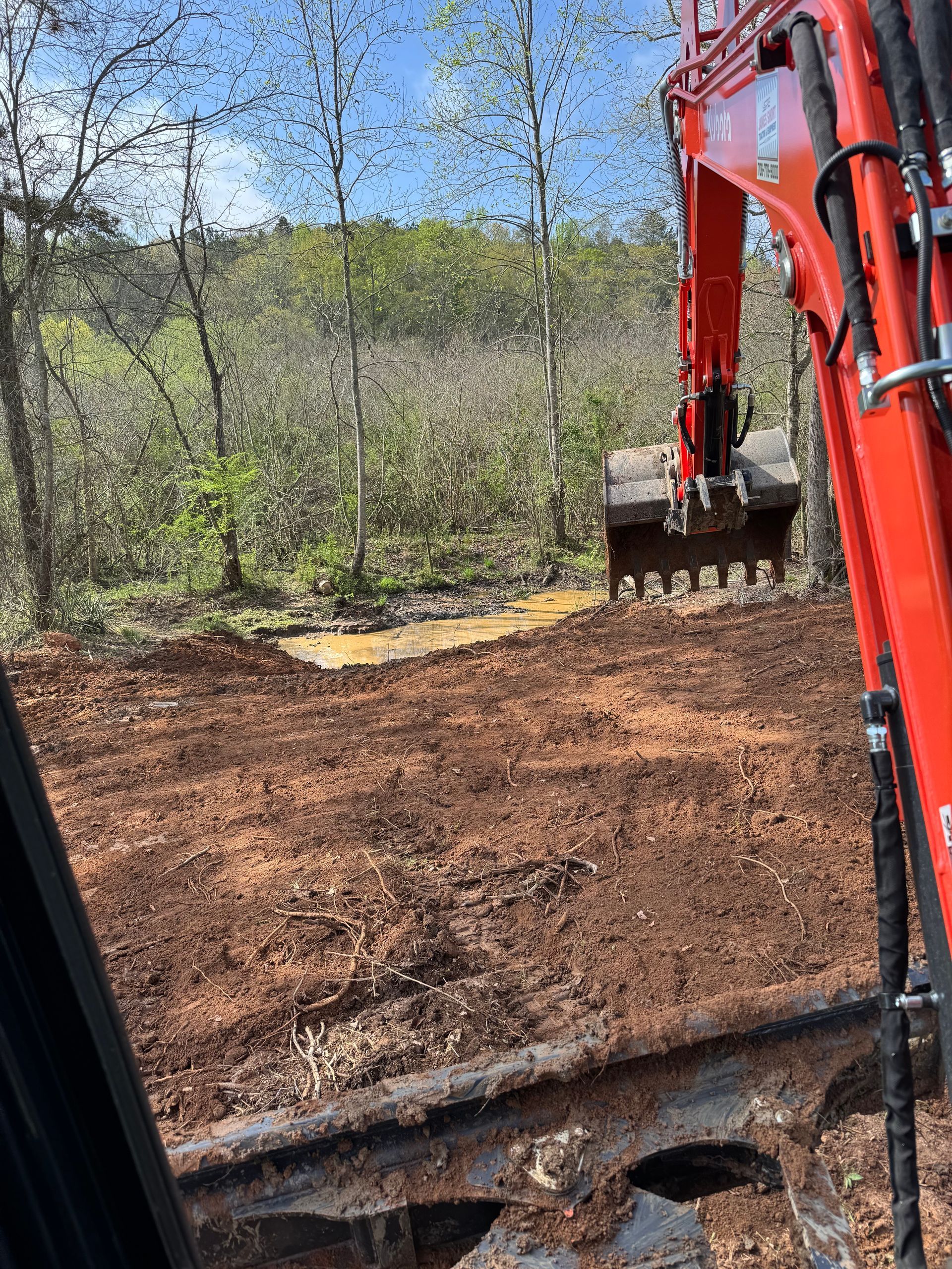 A red excavator is digging a hole in the ground in the woods.