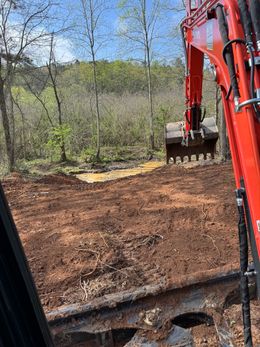 A red excavator is digging a hole in the ground in the woods.