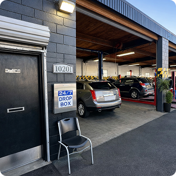 24/7 drop box outside a building with parked cars and a chair near the entrance | Costa Auto Care and TIre