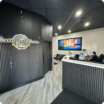 Modern auto glass repair shop reception with black-and-white counter and wall logo, two staff at desk, TV on wall | Costa Auto Care and TIre