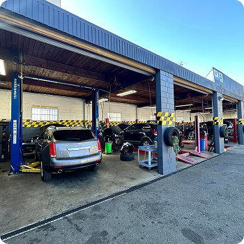 Auto repair shop with cars in service bays and a vehicle on a lift under a covered garage | Costa Auto Care and TIre