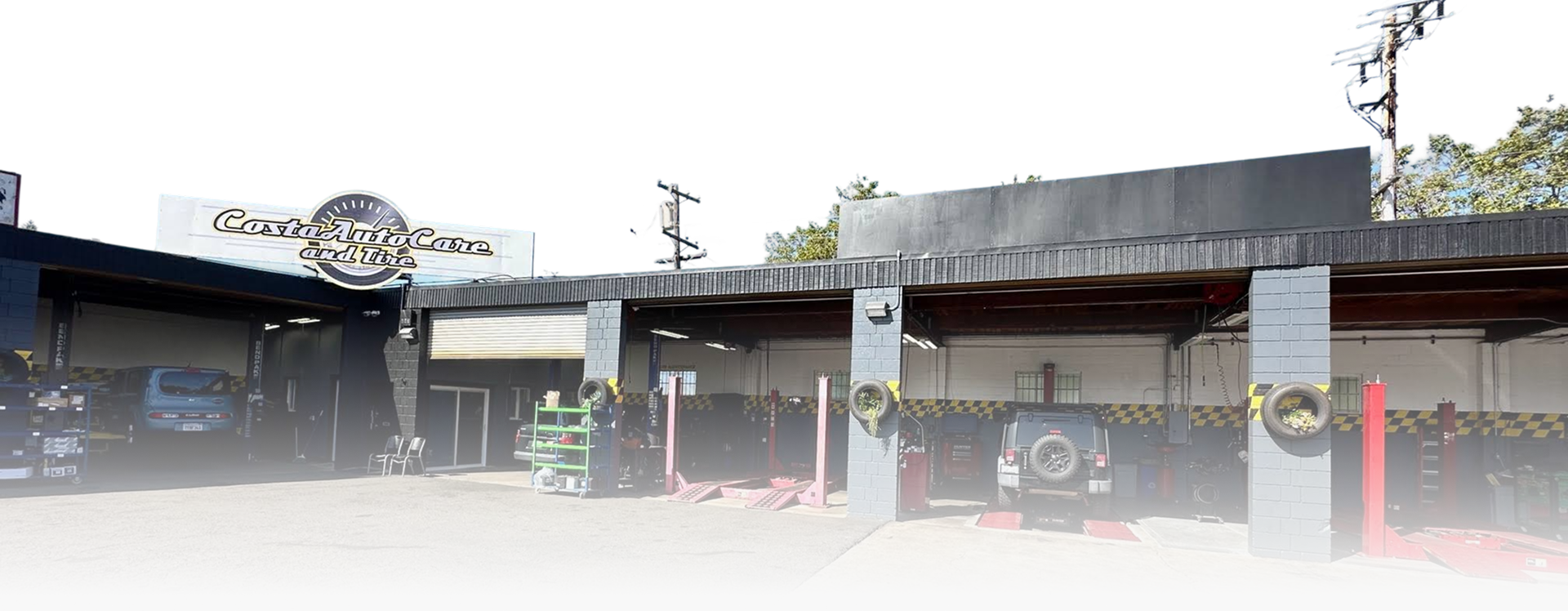 Low-rise commercial storefronts with signs, a parked white van, and red bollards in front | Costa Auto Care and TIre