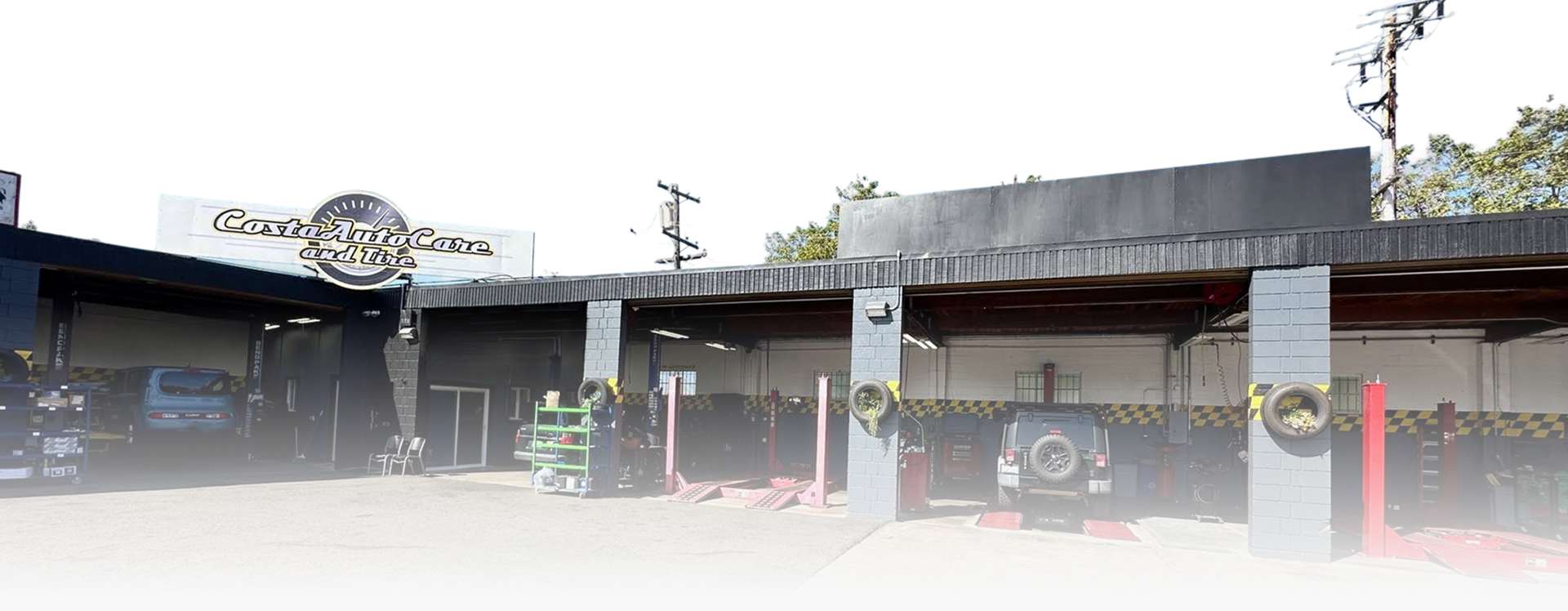 Low-rise commercial storefronts with signs, a parked white van, and red bollards in front | Costa Auto Care and TIre