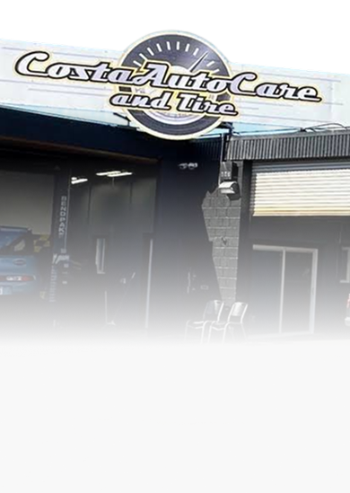 Low-rise commercial storefronts with signs, a parked white van, and red bollards in front | Costa Auto Care and TIre