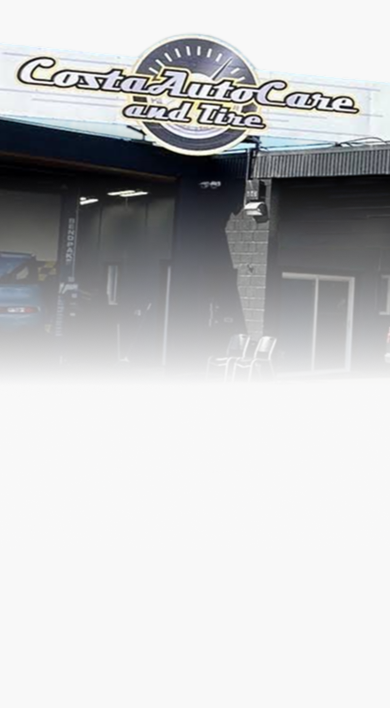 Low-rise commercial storefronts with signs, a parked white van, and red bollards in front | Costa Auto Care and TIre